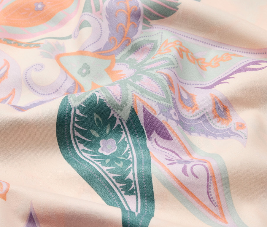 Detail látky s kvetinovým vzorom v zelenej, fialovej a oranžovej farbe.