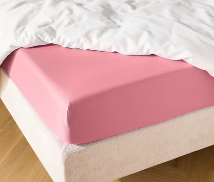 Detailný záber na posteľ s ružovou napínacou plachtou a bielou prikrývkou.
