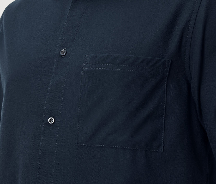 Detailný záber na tmavomodrú košeľu s krátkym rukávom, zapínanú na gombíky, s našitým náprsným vreckom.