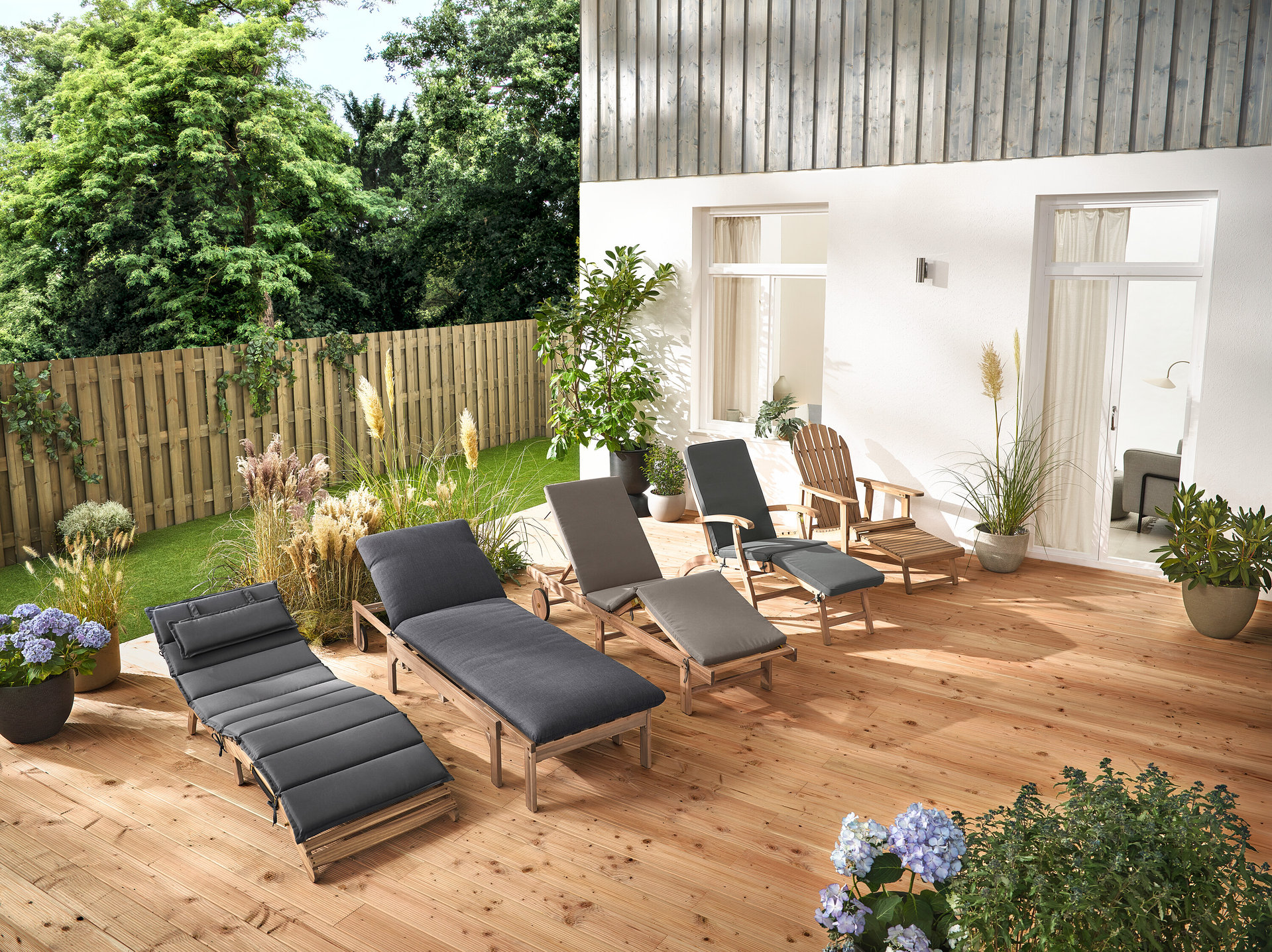 Na drevenej terase stojí niekoľko záhradných ležadiel a Adirondack relaxačné kreslo s vyťahovacou opierkou nôh z dreva.