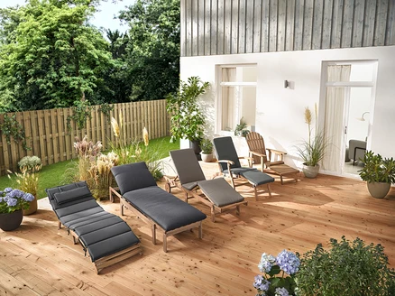 Na drevenej terase stojí niekoľko záhradných ležadiel a Adirondack relaxačné kreslo s vyťahovacou opierkou nôh z dreva.