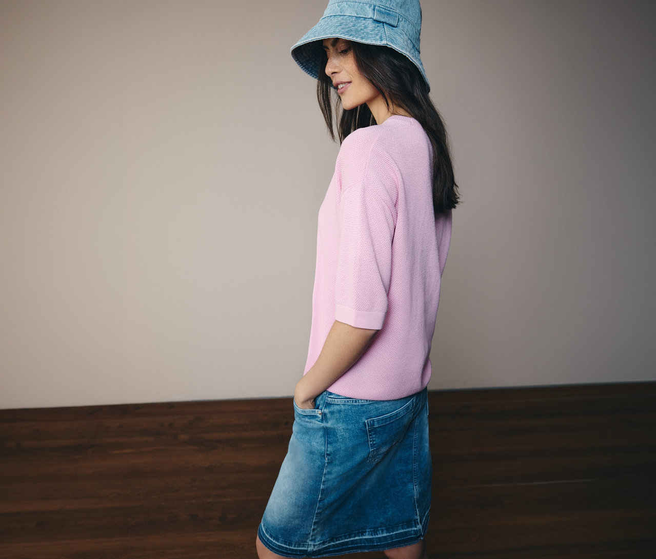 Žena s džínsovým klobúkom, ružovým pulóvrom s krátkym rukávom CECIL a džínsovou sukňou CECIL. Má ruky vo vreckách.