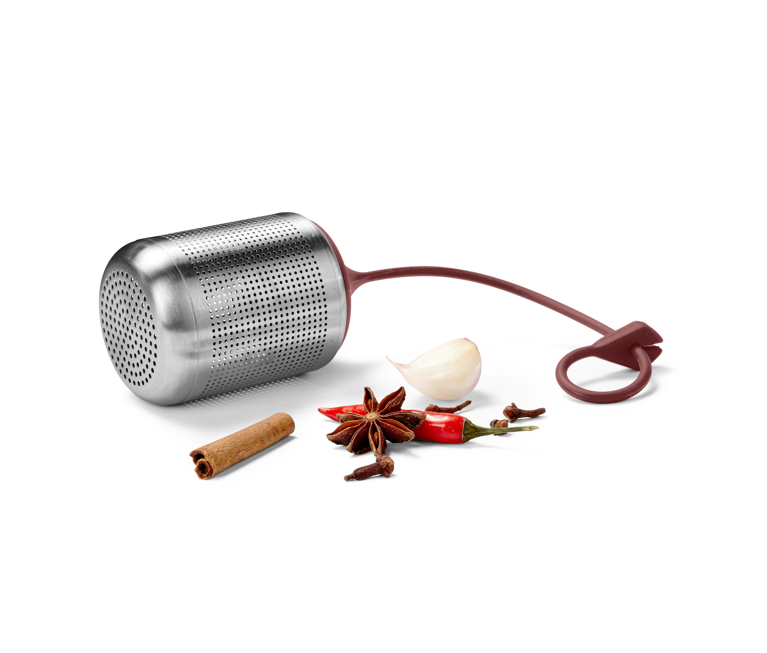 Kovové sitko na korenie leží na bielom povrchu vedľa korenia.