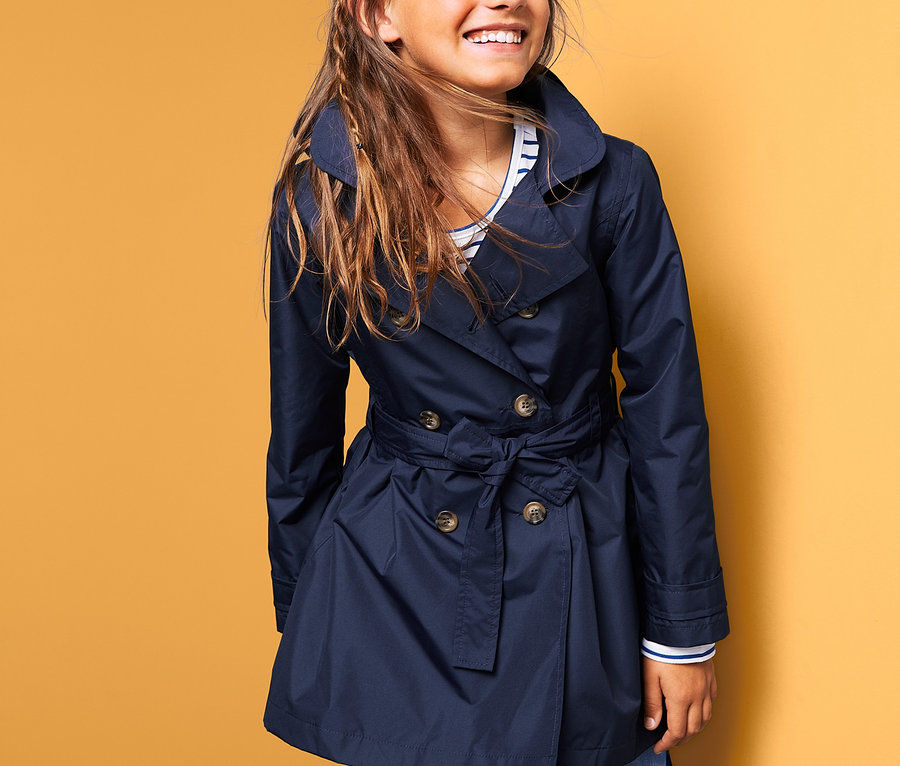 Usmievajúce sa dievča má na sebe tmavomodrý trenčkot do každého počasia.