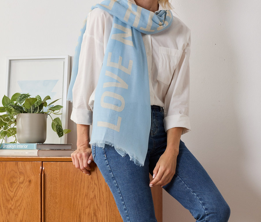 Blondínka pózuje so svetlomodrou tkanou šálou so statement potlačou.