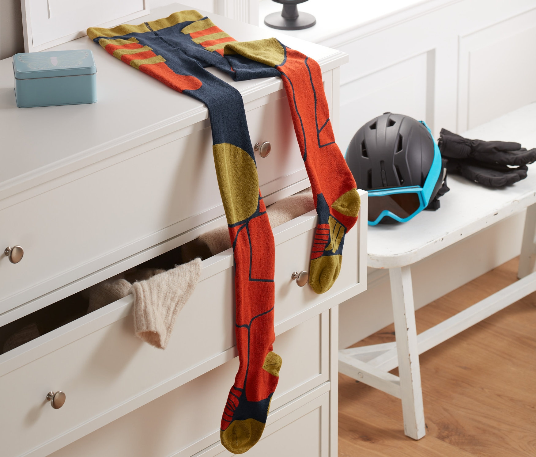 Lyžiarske pančuchové nohavice ležia na bielej komode vedľa rámu s písmenom T. V pozadí je okno a glóbus.