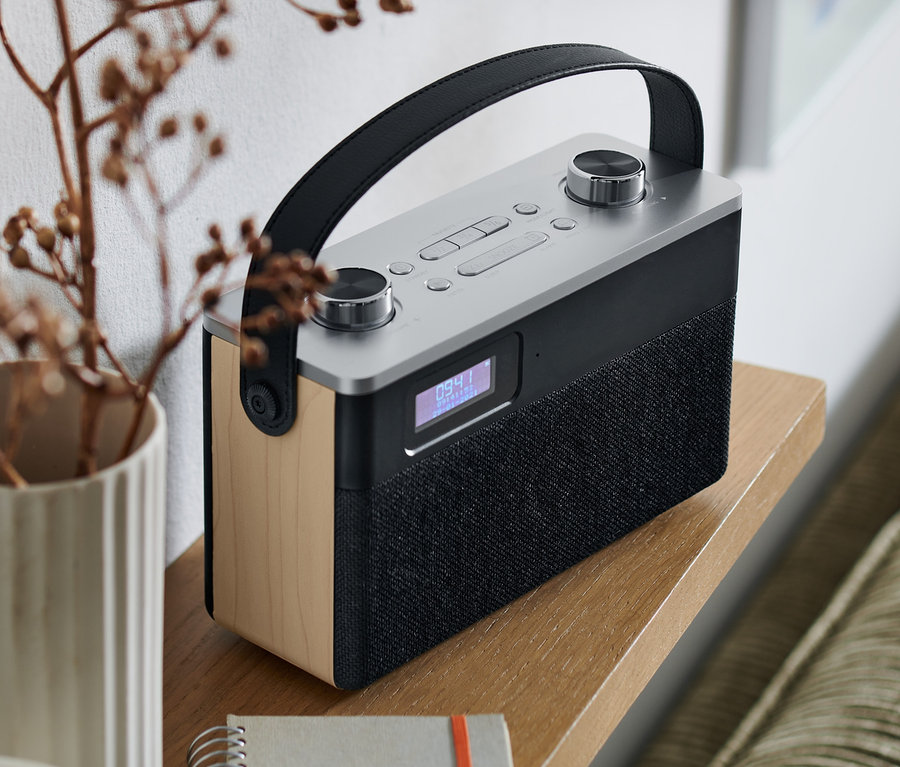 DAB+/FM digitálne rádio s Bluetooth® na drevenej poličke vedľa vázy s vetvičkami a poznámkového bloku.