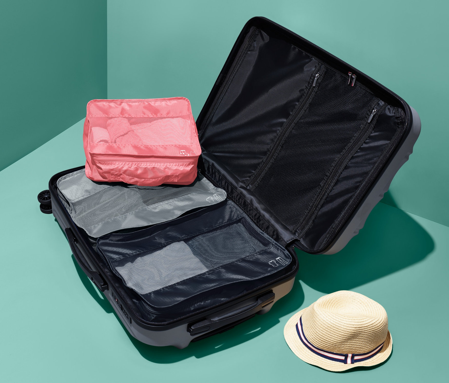 Otvorený kufor s cestovnými úložnými taškami, 3 ks, a klobúk.