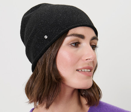 Žena s hnedými vlasmi nosí trblietavú čiapku typu beanie v čiernej farbe.