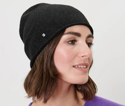 Žena s hnedými vlasmi nosí trblietavú čiapku typu beanie v čiernej farbe.