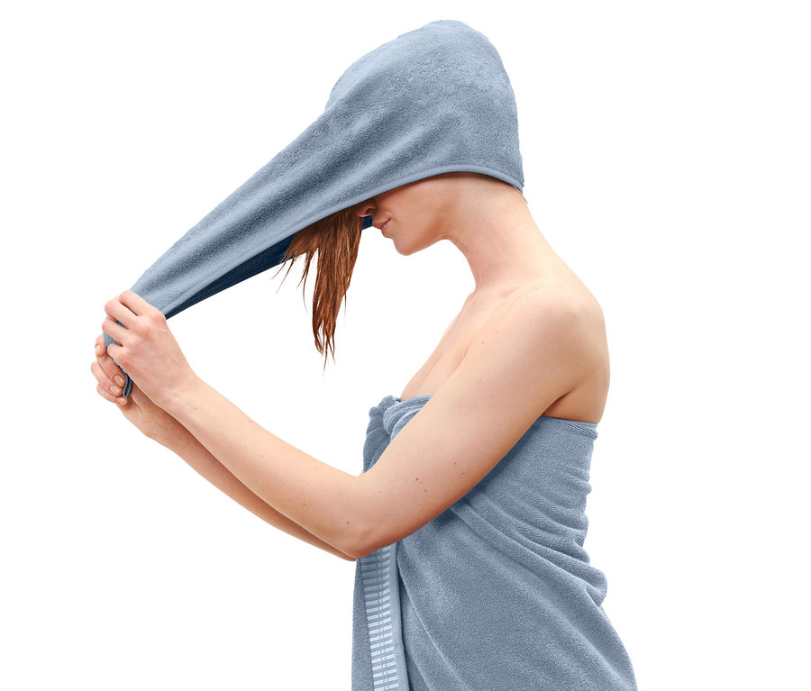 Žena si dáva na hlavu svetlomodrý uterákový turban.