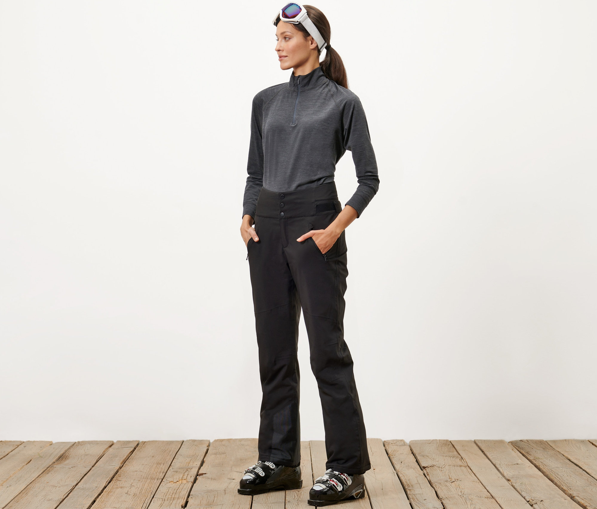 Žena stojí a má ruky vo vreckách lyžiarskych nohavíc s vysokým pásom.