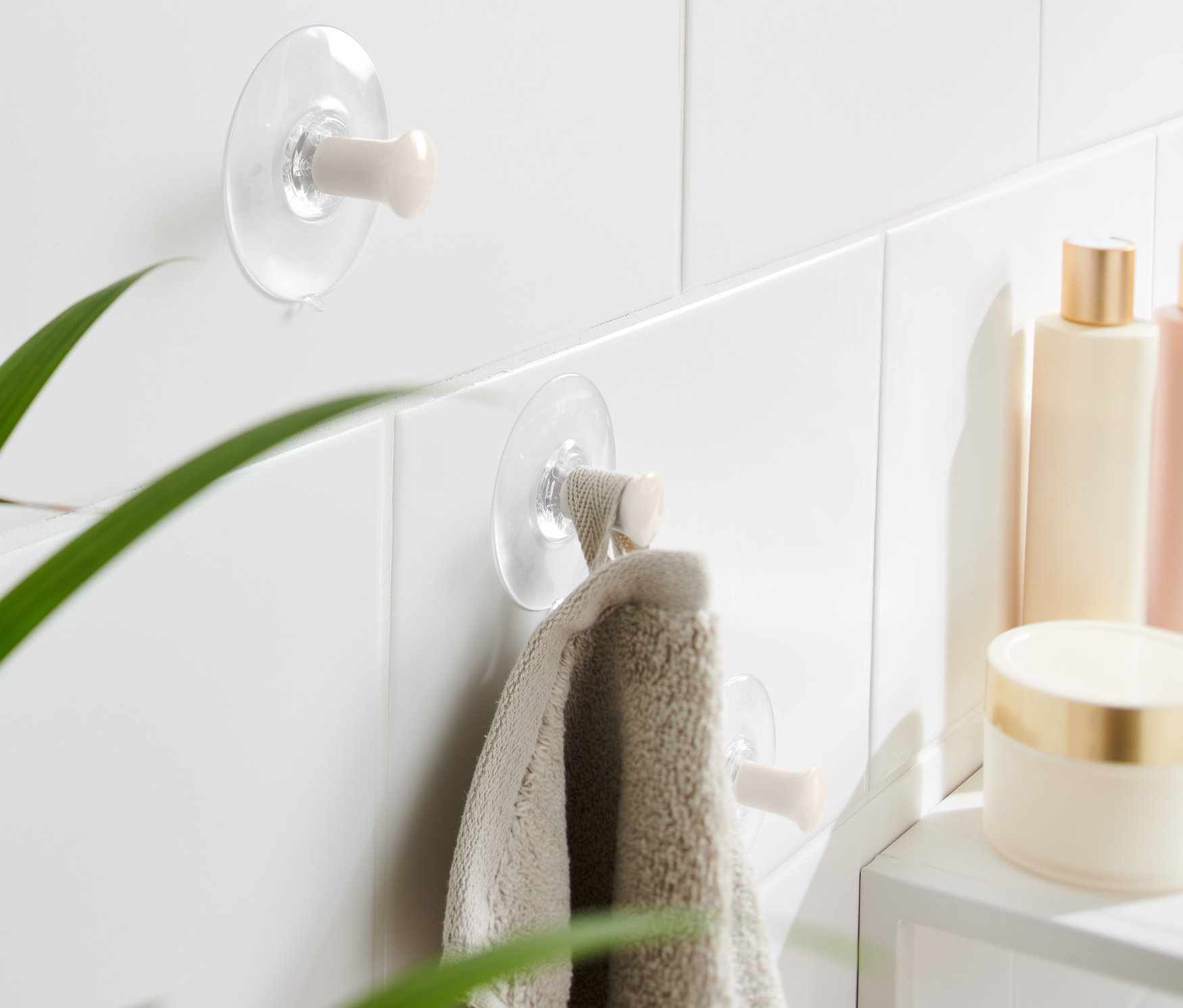 Na bielych dlaždiciach sú pripevnené dva háčiky s prísavkou, na jednom z nich visí uterák.