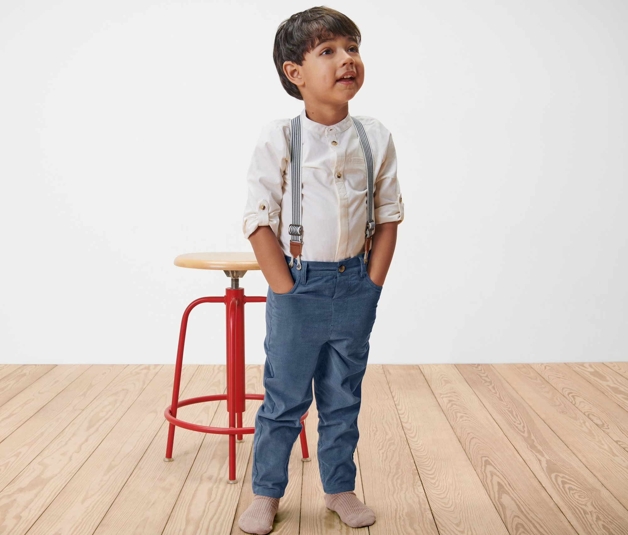 Chlapec stojí s rukami vo vreckách a má na sebe detské menčestrové nohavice s odnímateľnými trakmi.