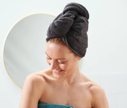 Žena s uterákovým turbanom antracitovej farby na hlave a modrým uterákom omotaným okolo tela.