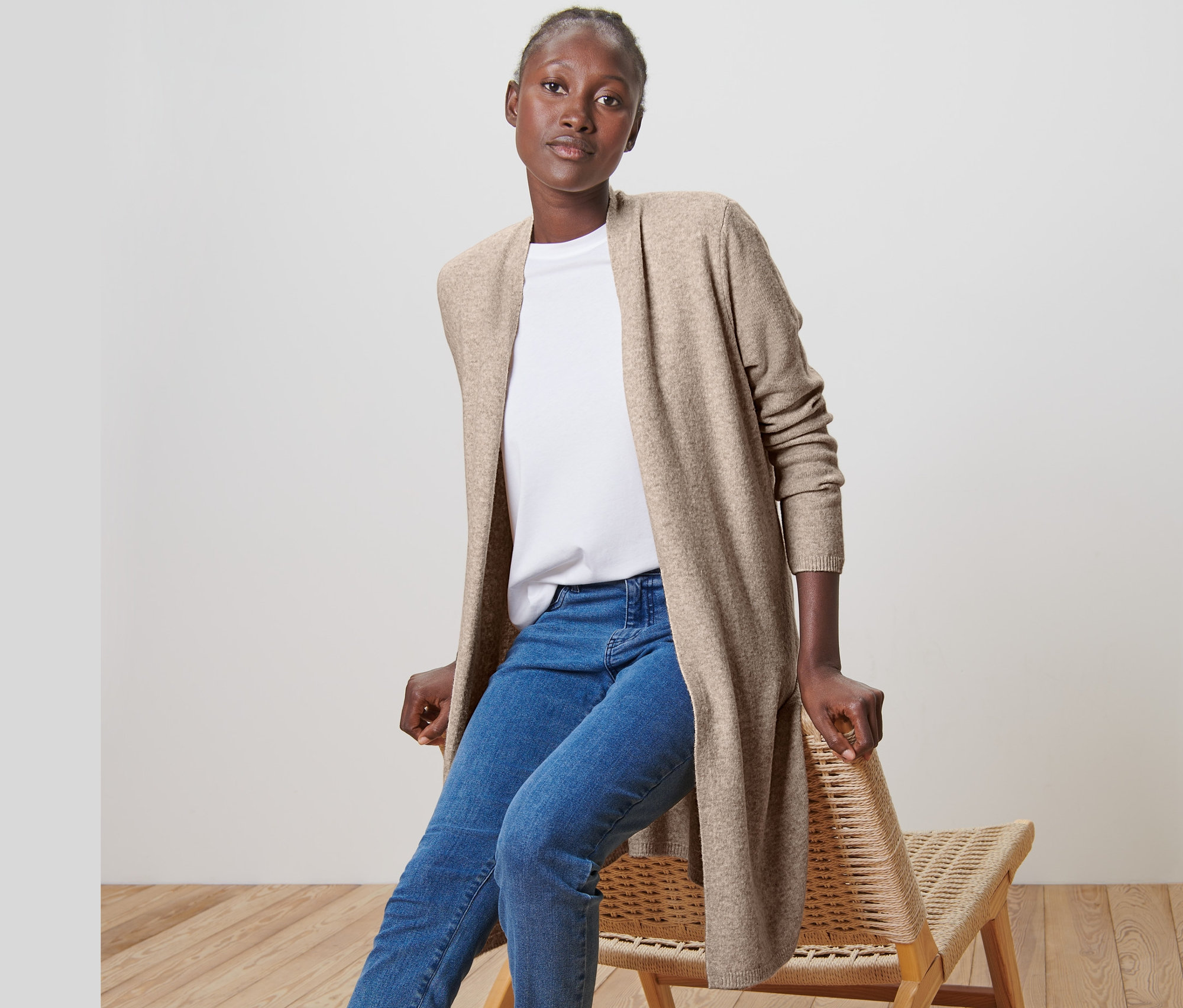 Žena sedí na stoličke a má na sebe dlhý kardigán bez zapínania.