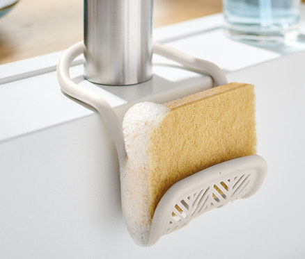 Držiak na hubku s hubkou pripevnený na kohútiku v bielom dreze.