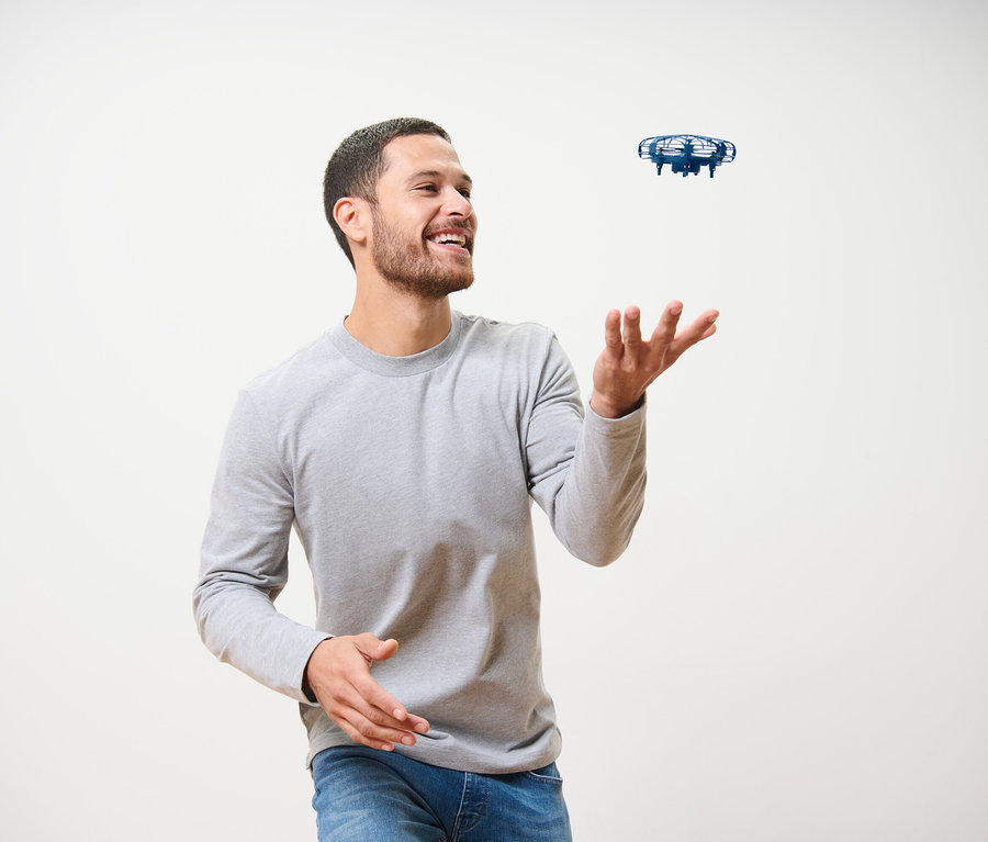 Muž sa smeje a hrá sa s modrým minidronom »UFO«.