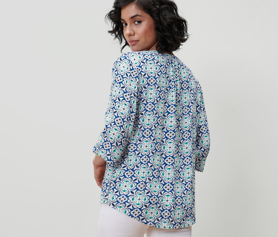 Žena sa pozerá cez plece a má na sebe tunikovú blúzku s celoplošnou potlačou.