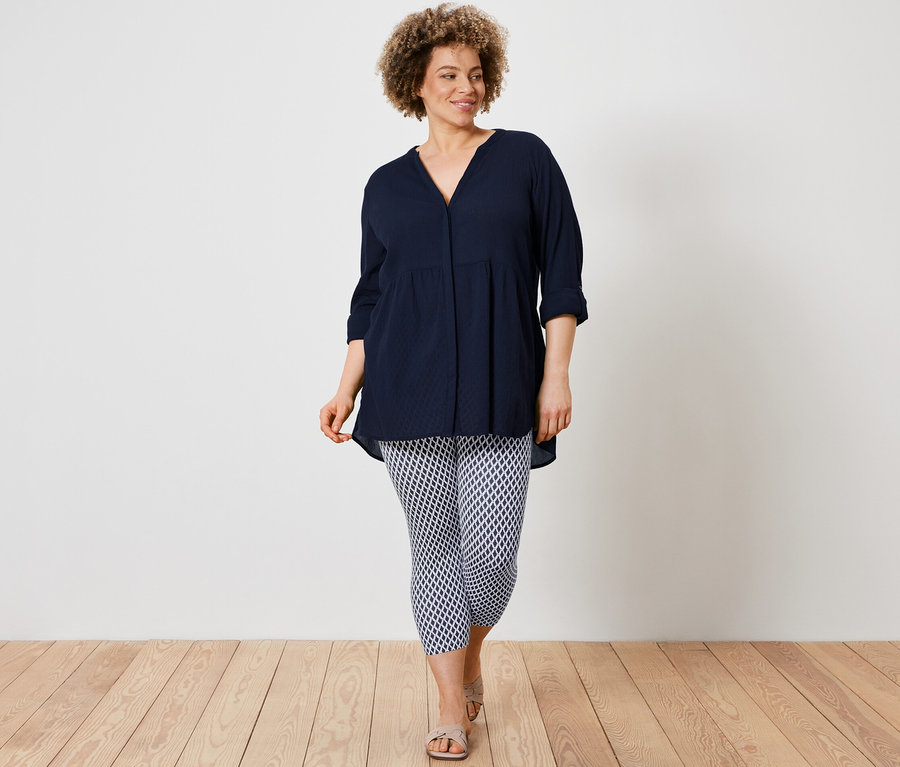 Žena má na sebe dlhú blúzku a potlačené 3/4 legínsy.