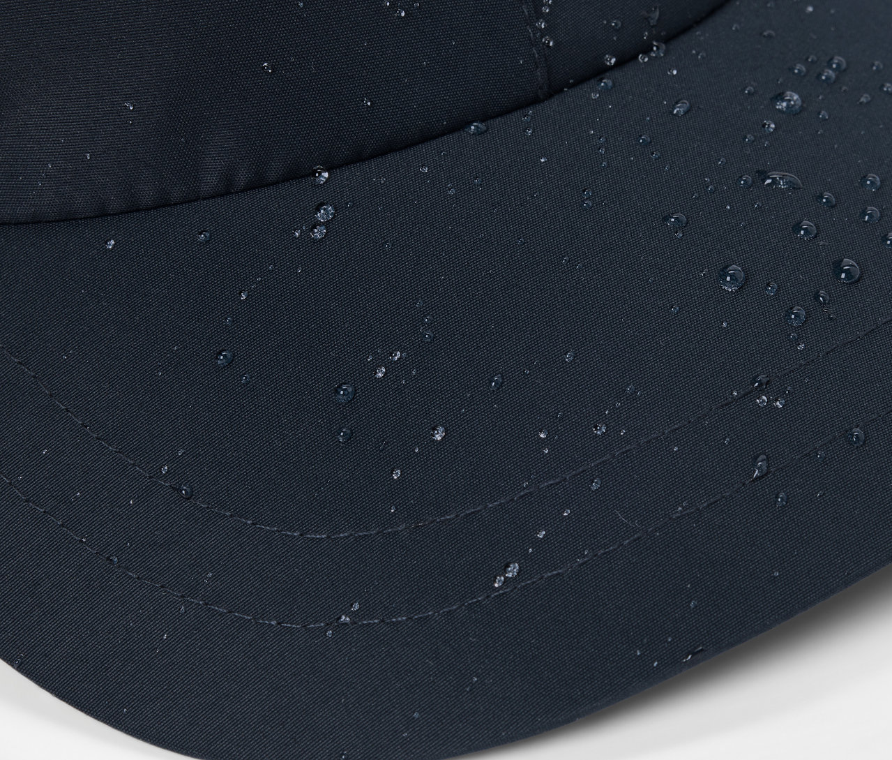 Detailný záber na čiernu šiltovku do každého počasia s kvapkami vody na povrchu.