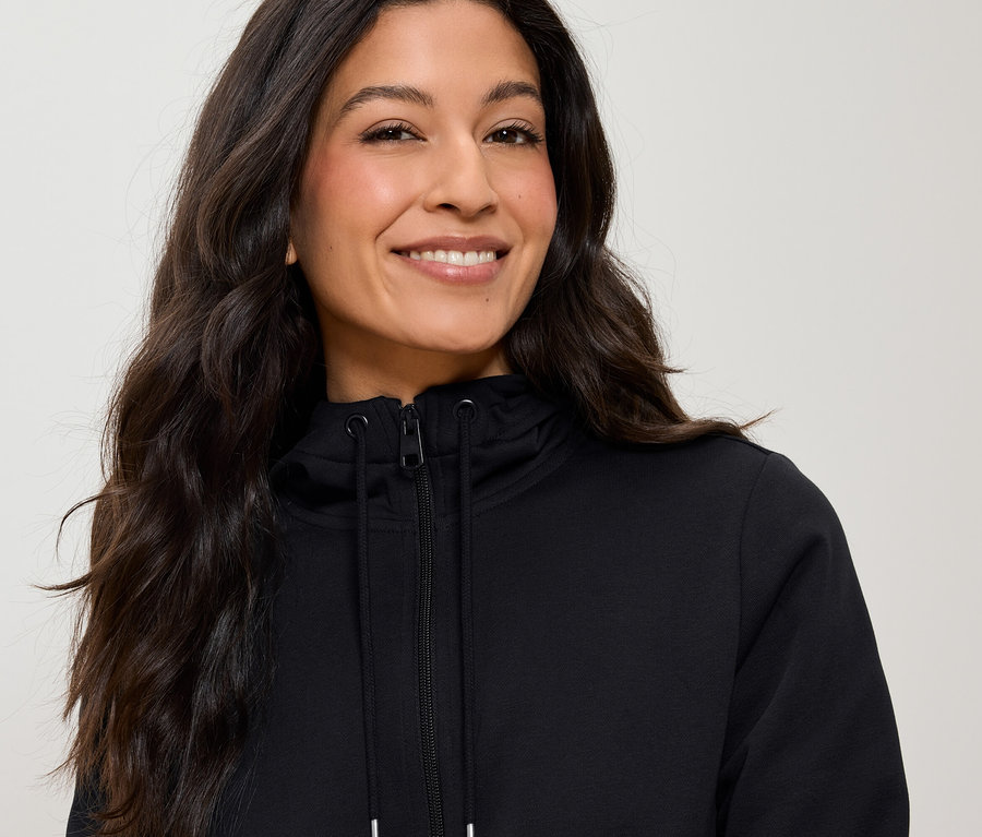 Portrét ženy s dlhými hnedými vlasmi, ktorá má na sebe čiernu mikinu na zips.