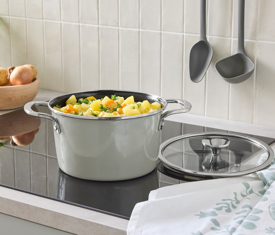 Na varnej doske stojí hrniec s pokrievkou a zeleninou. V pozadí je misa so zemiakmi a zavesené naberačky.