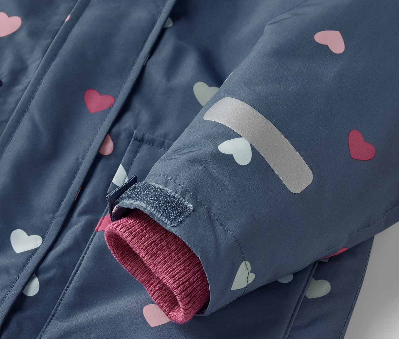 Detail modrej 2-dielnej detskej zimnej kombinézy s ružovými a bielymi srdiečkami.