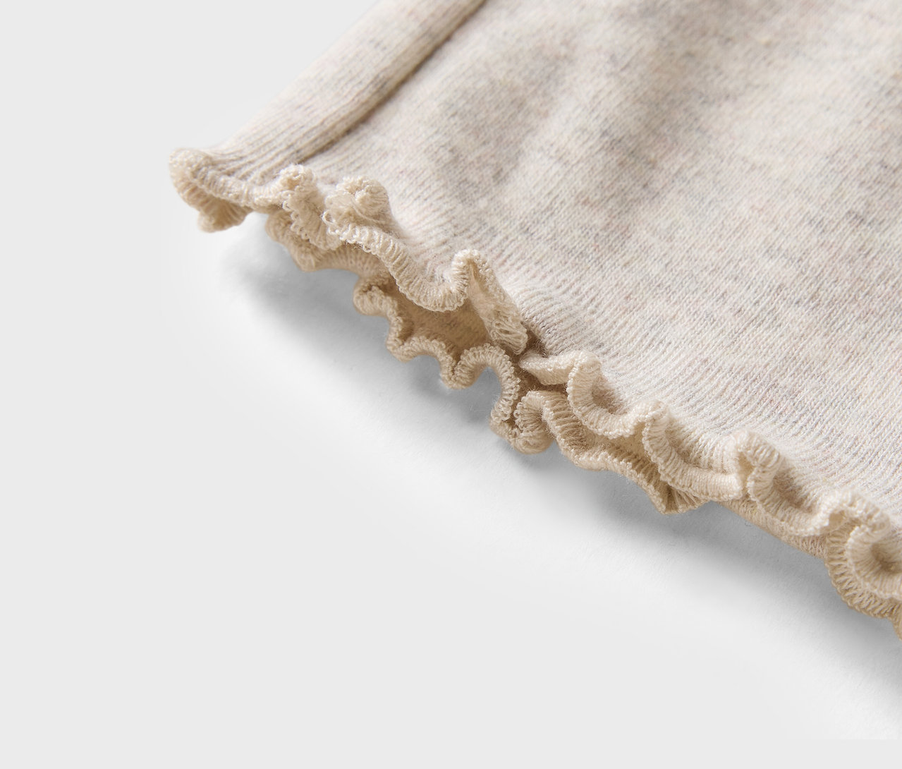 Detail béžového svetra s volánovým lemom.