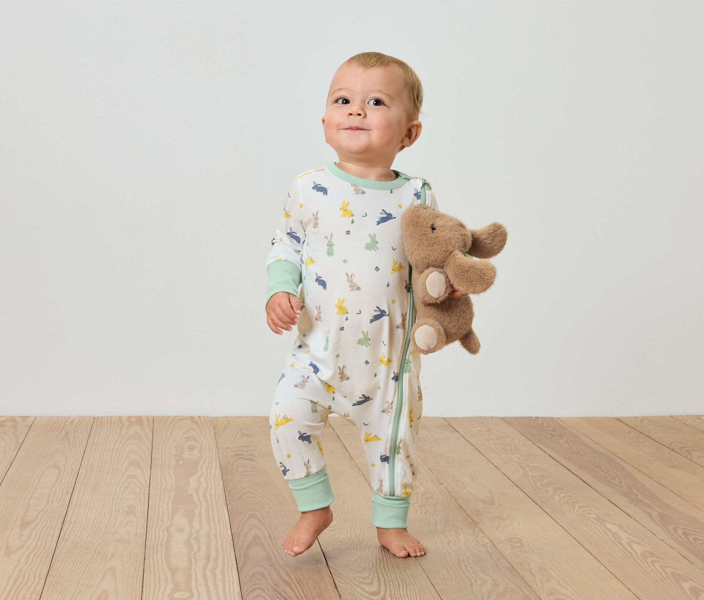 Dieťa stojí na drevenej podlahe a drží plyšového slona.