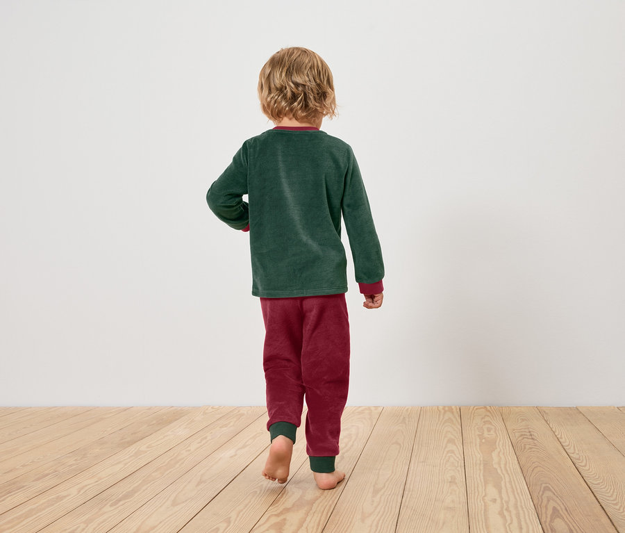 Chlapec v zelenom pyžamovom tope a vínových pyžamových nohaviciach kráča naboso po drevenej podlahe.