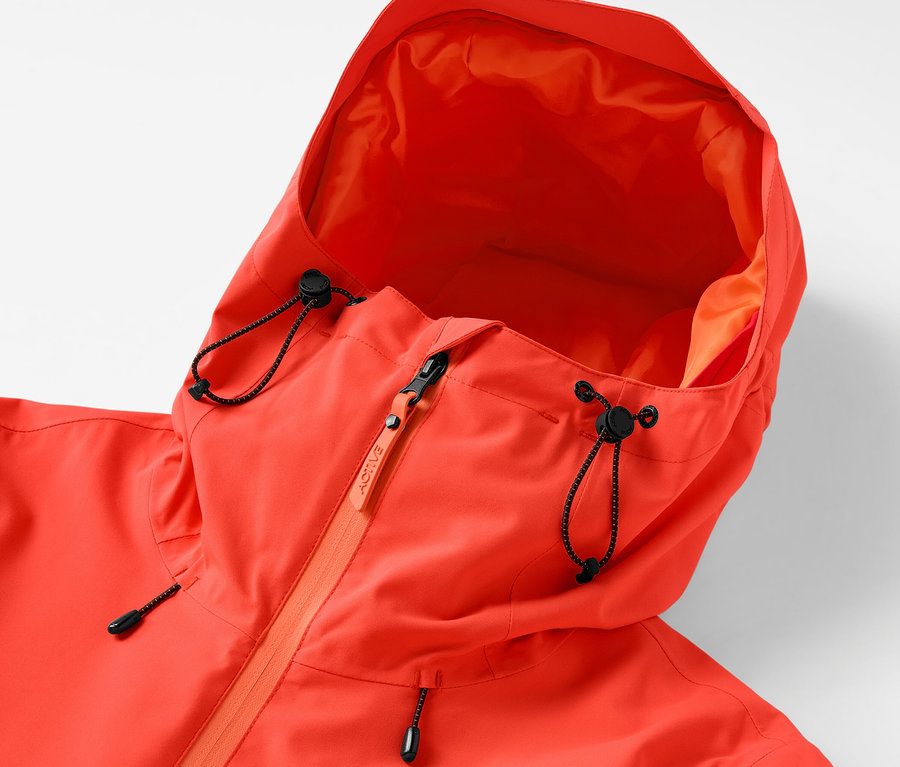 Detail oranžovej bundy s kapucňou so sťahovacou šnúrkou a zipsom.