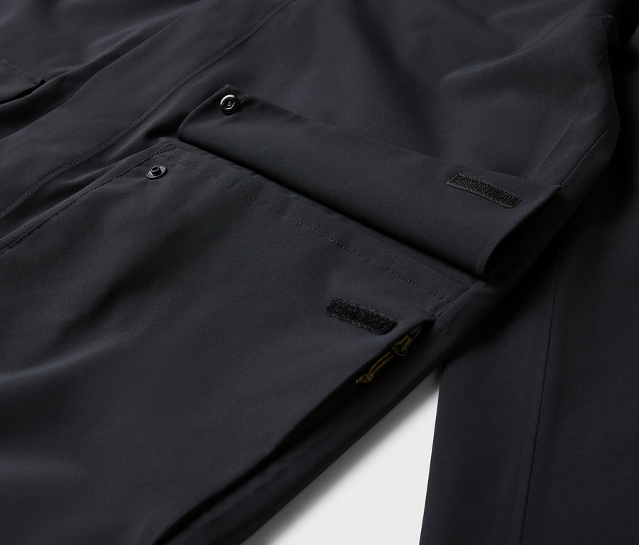 Detail čiernej bundy s vreckami a gombíkmi.