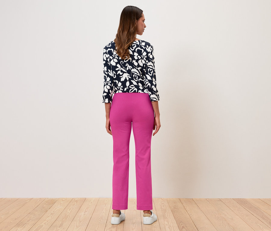 Žena stojí chrbtom, má na sebe kvetovanú blúzu a ružové nohavice.
