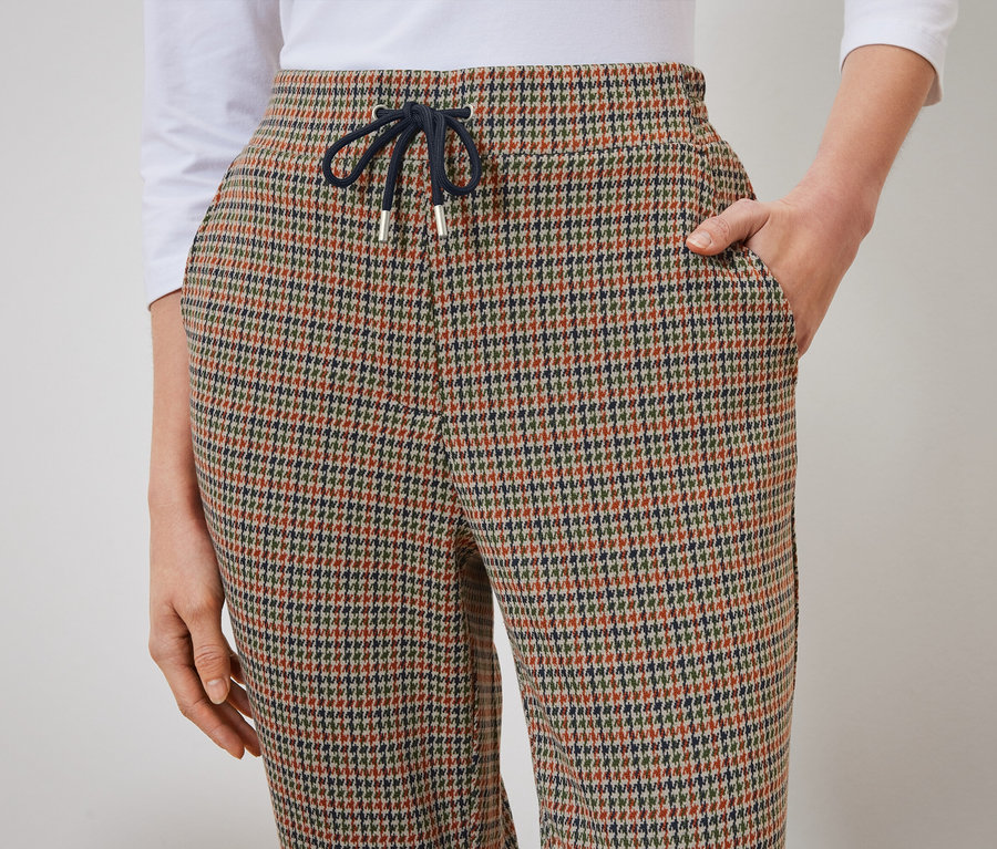 Detail dámskych nohavíc so vzorom kohútej stopy s rukou vo vrecku.