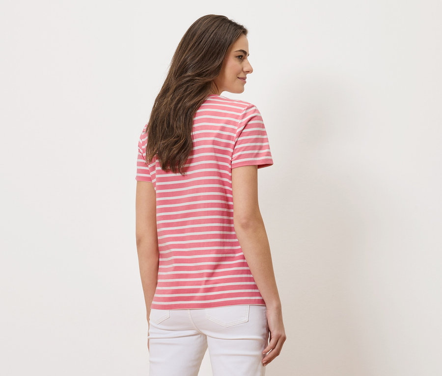 Žena zozadu, má na sebe ružovo-biele pruhované tričko a biele džínsy.