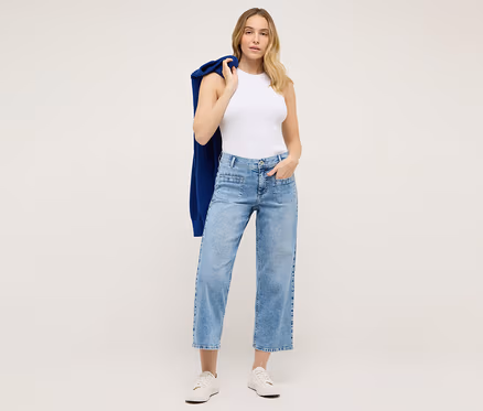 Žena v svetlomodrých nohaviciach Angels Denim »Linn Smart« Culotte, bielom tope a modrom svetri prehodenom cez rameno pózuje na svetlom pozadí.