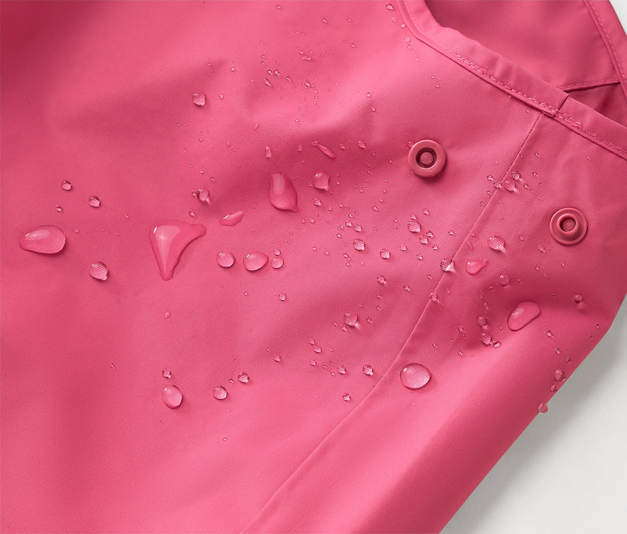 Detail ružovej bundy s kvapkami vody a dvoma patentkami.
