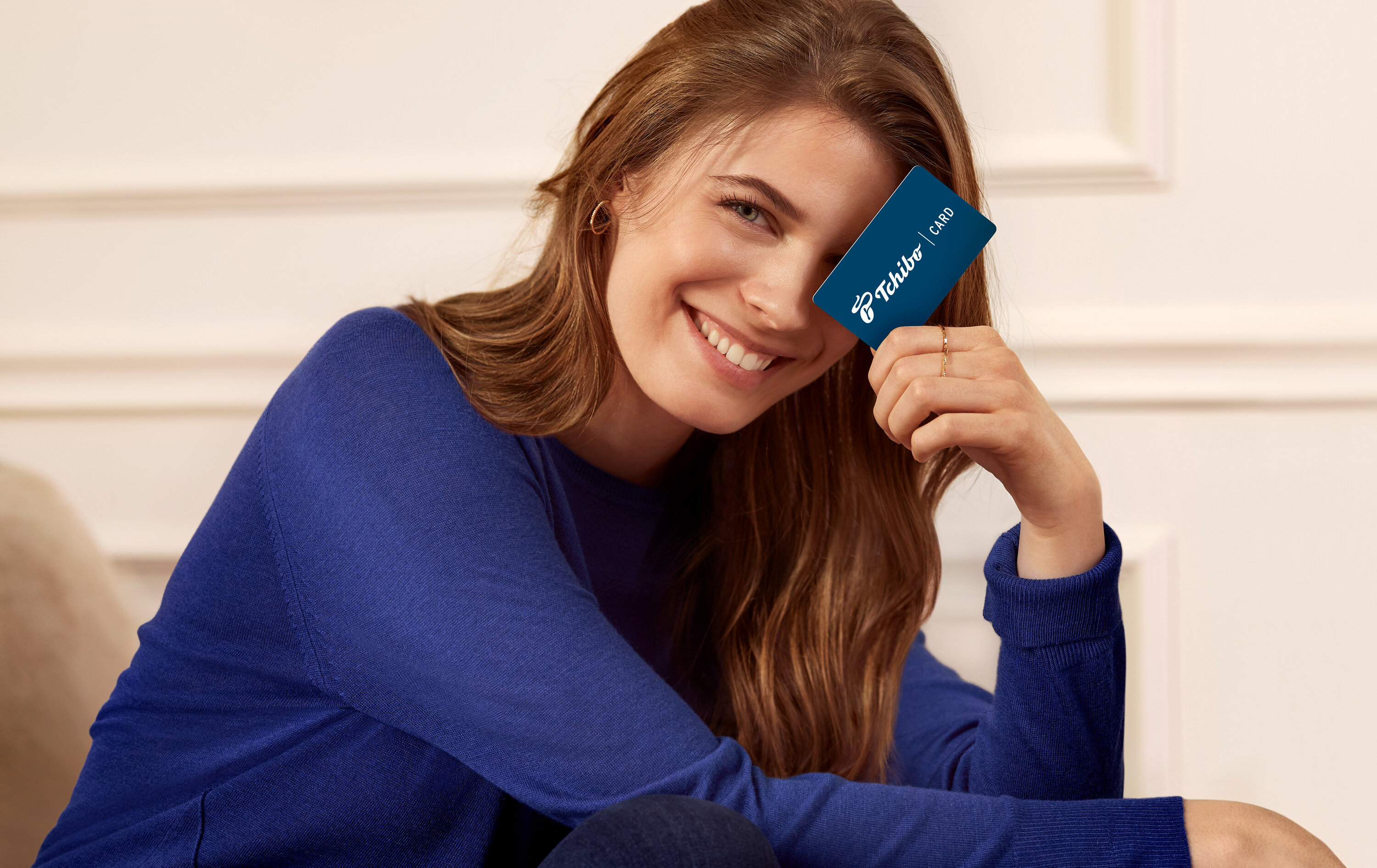 Usmievajúca sa žena drží kartu Tchibo pred okom.