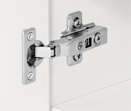 Detail strieborného pántu na bielej skrinke.