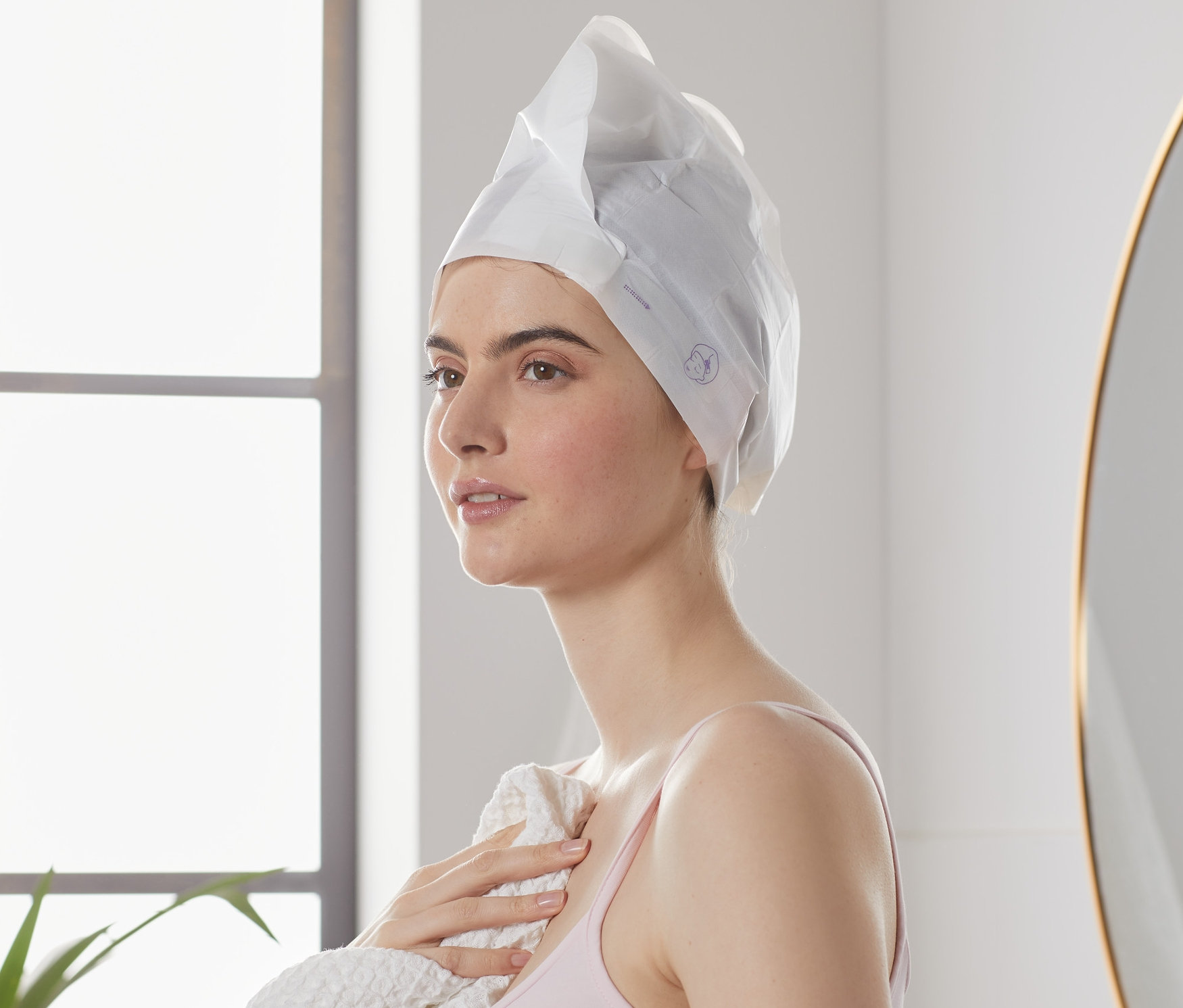 Žena s hrejivou textilnou maskou na vlasy (2-dielna súprava) a uterákom v kúpeľni.