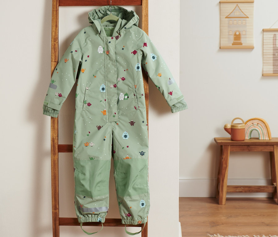 Zelený overal do dažďa visí na drevenom rebríku.