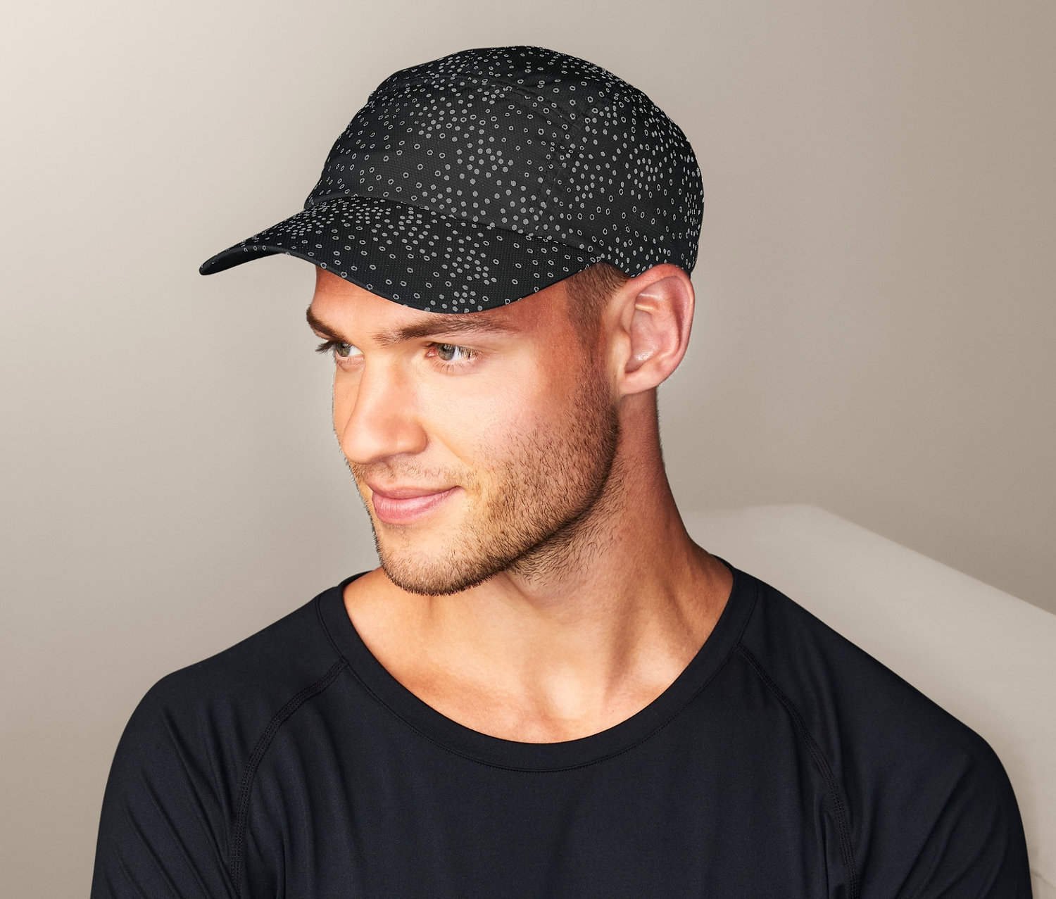 Muž so skríženými rukami nosí čiernu športovú čiapku Reflexná športová šiltovka a čierne tričko s dlhým rukávom.