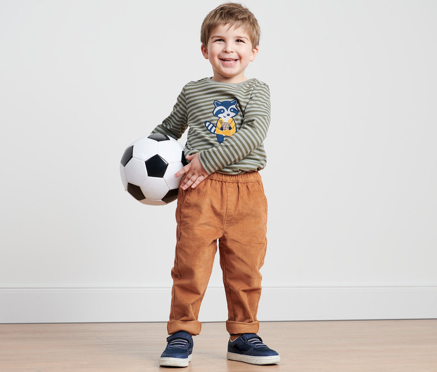 Chlapec drží futbalovú loptu a má na sebe hnedé detské kordové pull-on nohavice.