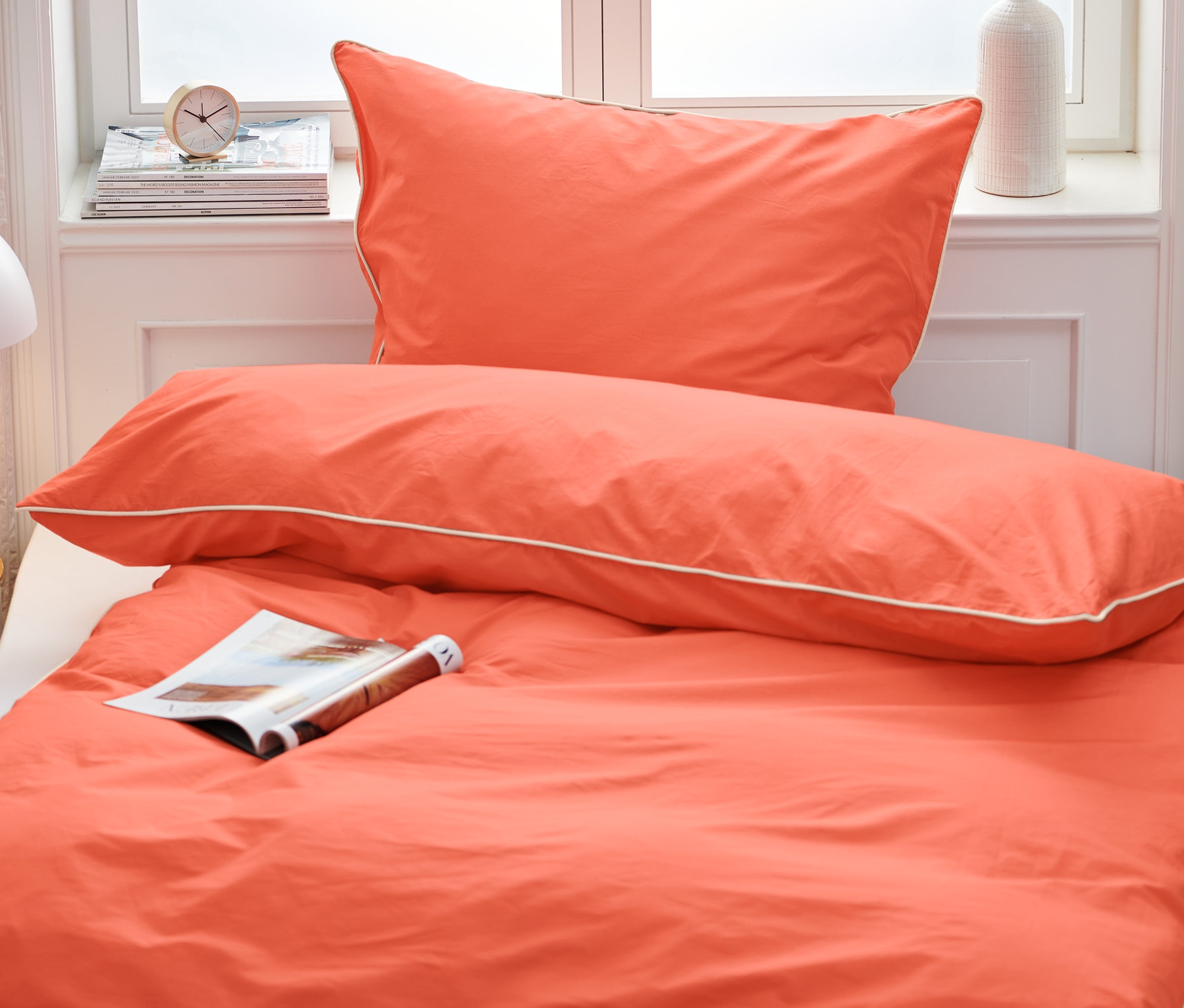 Oranžové prémiové bavlnené posteľné obliečky štandardnej veľkosti na posteli s časopisom.
