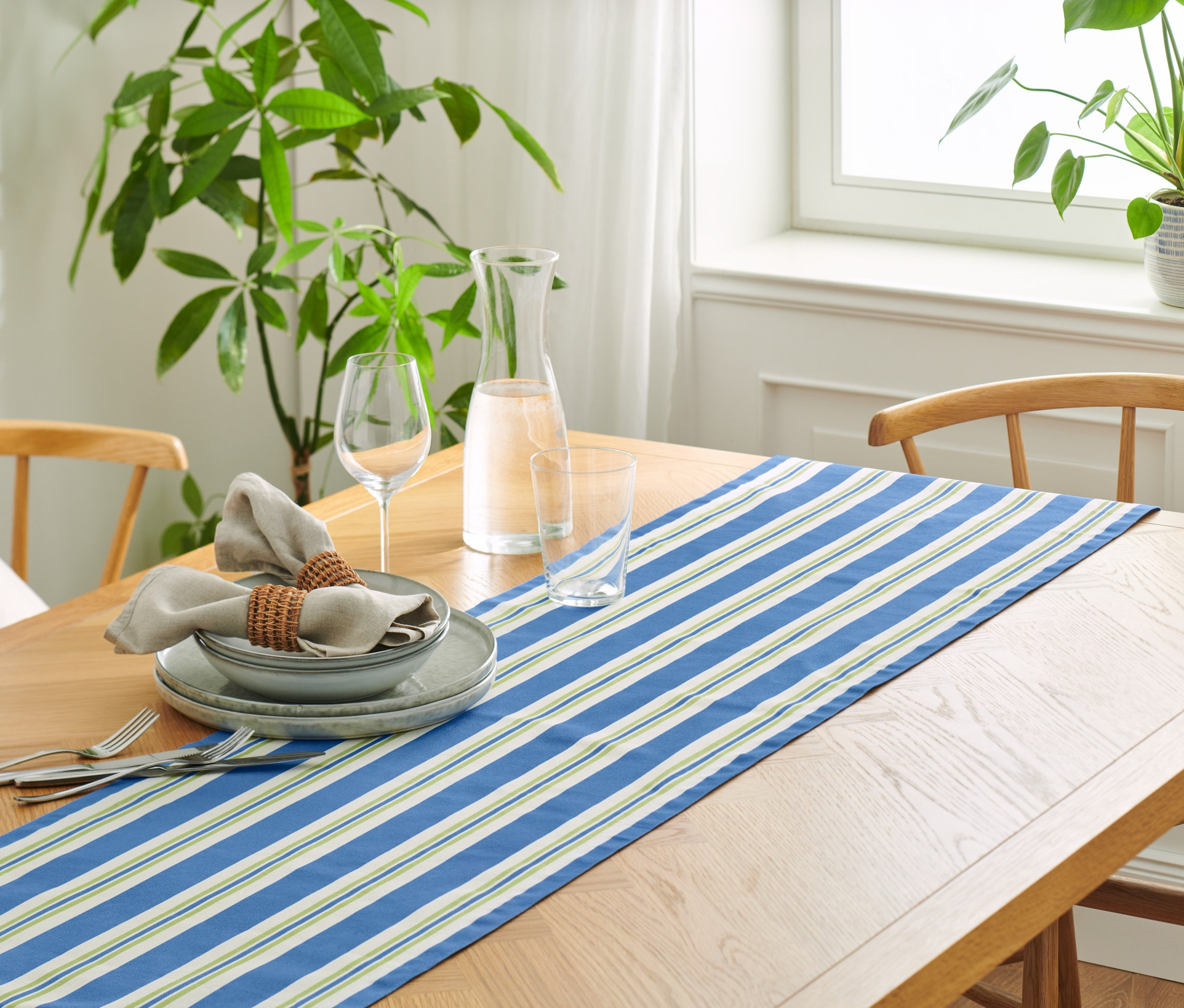 Prestretý stôl s bavlneným behúňom s prúžkami, taniermi, pohármi a ľanovými obrúskami.
