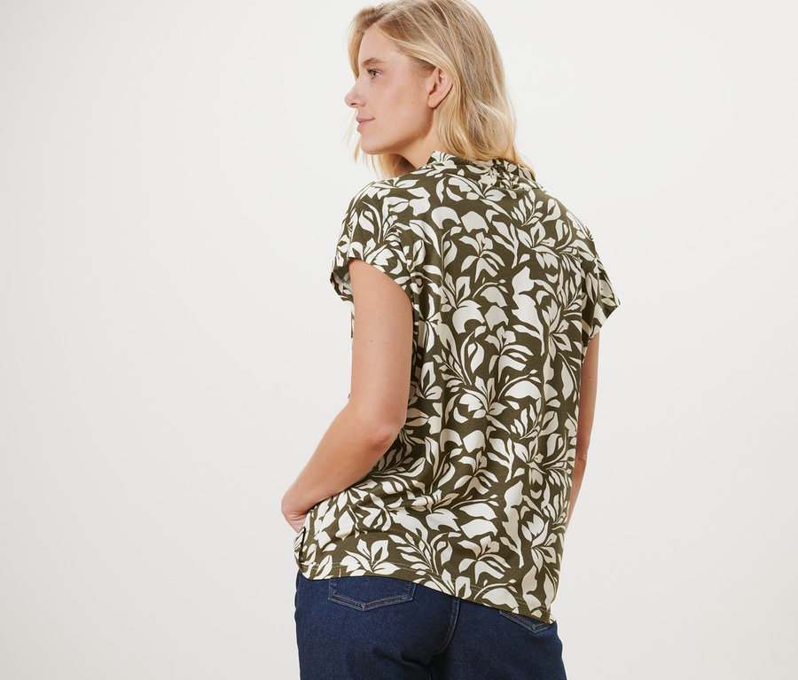 Žena stojí chrbtom a má na sebe blúzkové tričko s potlačou s výstrihom do V a džínsy.