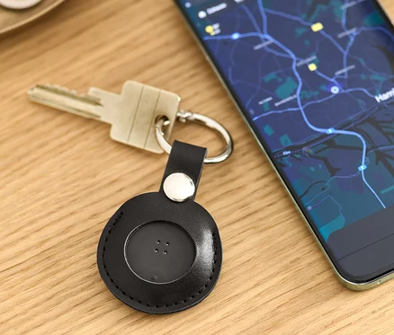 Na stole ležia kľúče s čiernym Smart Tracker s príveskom a mobilný telefón s mapou.