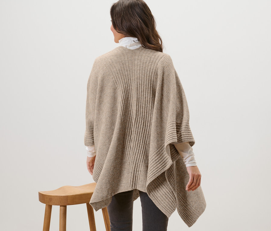 Žena stojí chrbtom a má na sebe pletenú pelerínu.