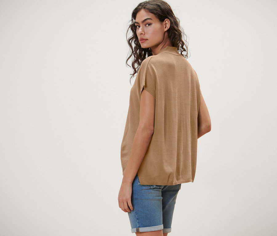 Žena sa pozerá cez plece a má na sebe béžový kardigán s krátkymi rukávmi.